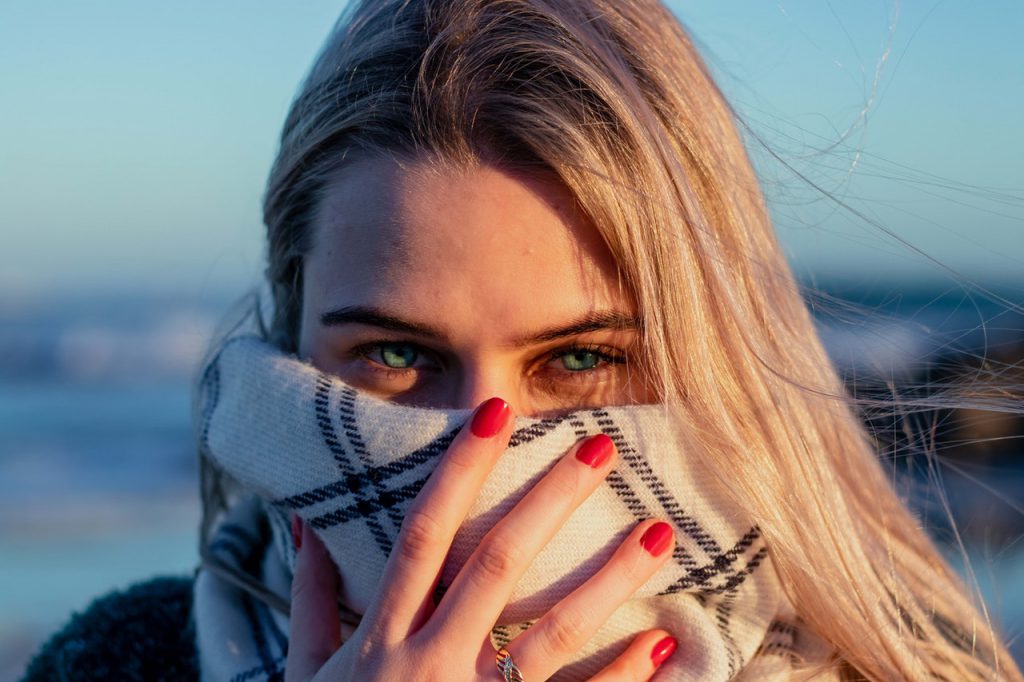 Young lady covering her mouth with a scarf while smiling.